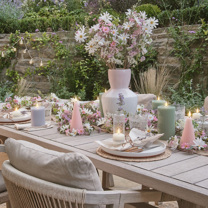 Set outdoor dining table with LED candles, flower garlands and a bouquet of pink and white flowers in a vase