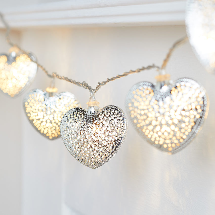Silver filigree heart fairy lights draped on a mantlepiece