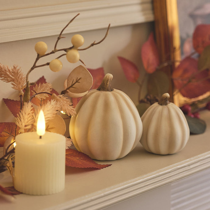 White porcelain pumpkins, LED votive candle, and autumnal garland on a mantle