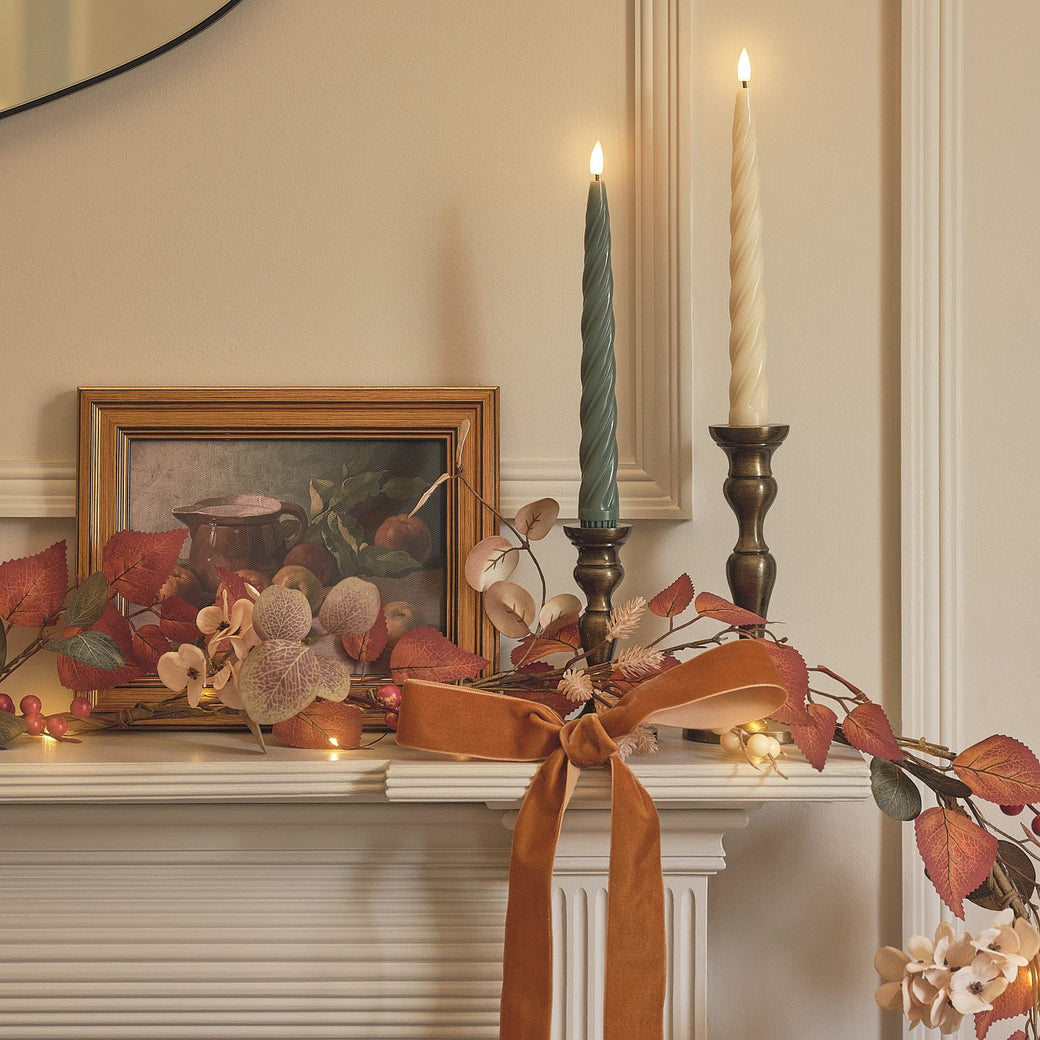 An autumnal mantelpiece decorated with foliage, taper candles, and a ribbon