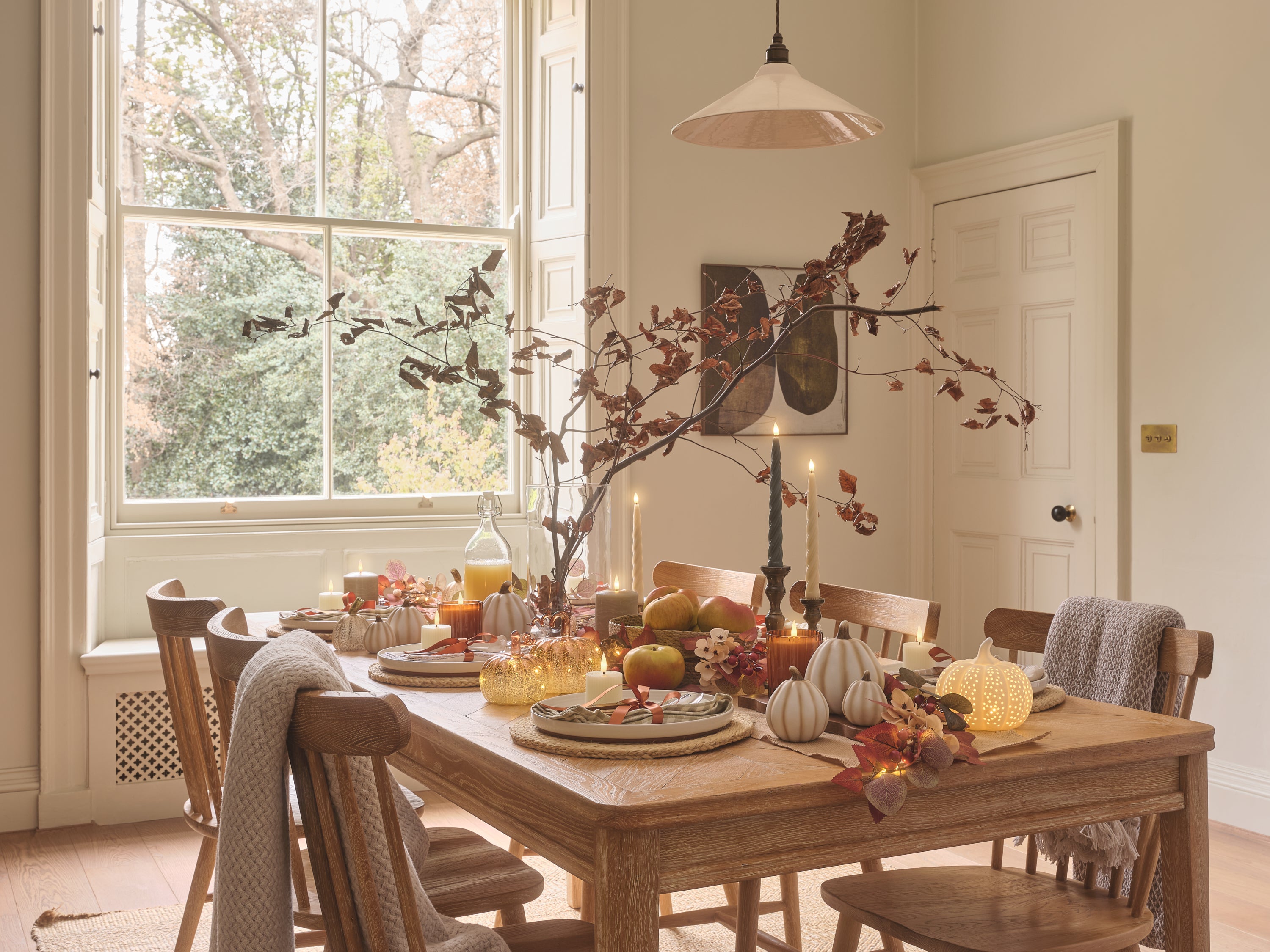 A dining table set with LED candles, porcelain and glass pumpkins, and autumnal foliage