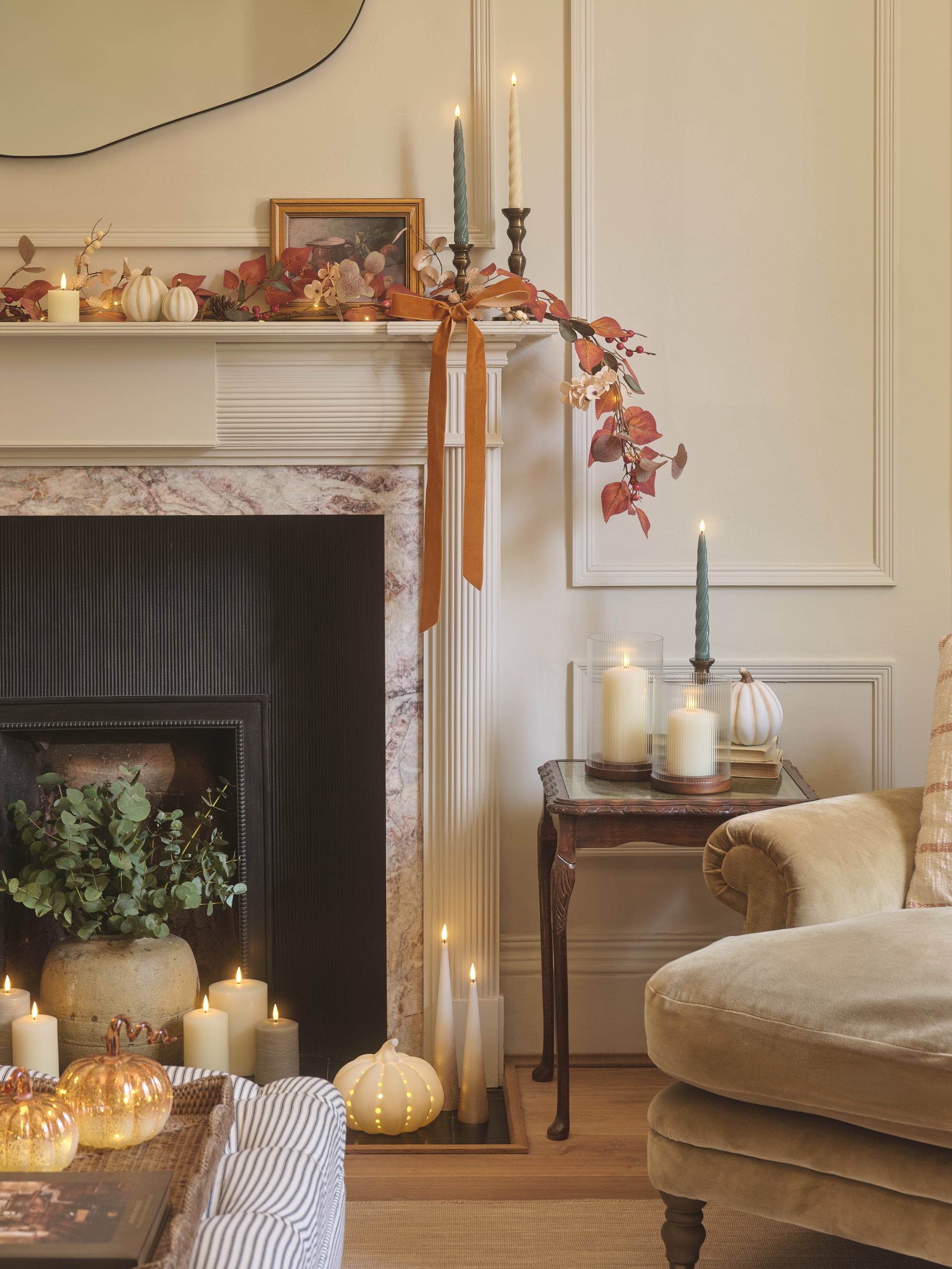 A fireplace decorated with LED candles, glass and porcelain pumpkins, and autumnal garland