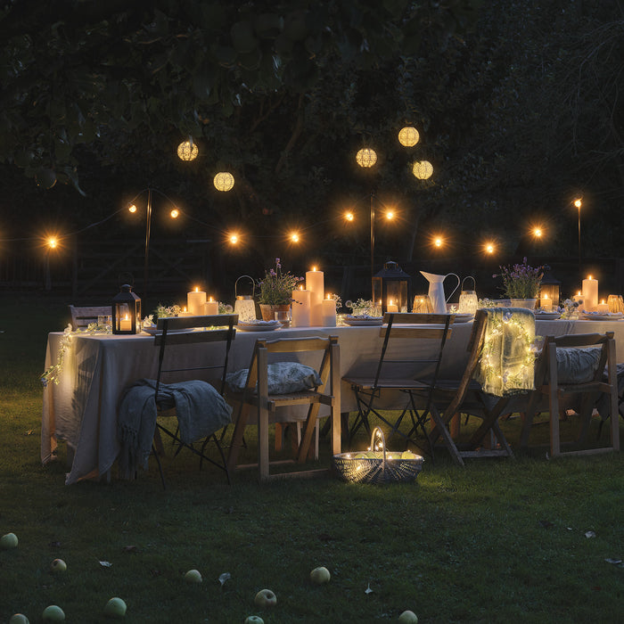 Night time outdoor dining table set with LED candles and lanterns, underneath festoon lights