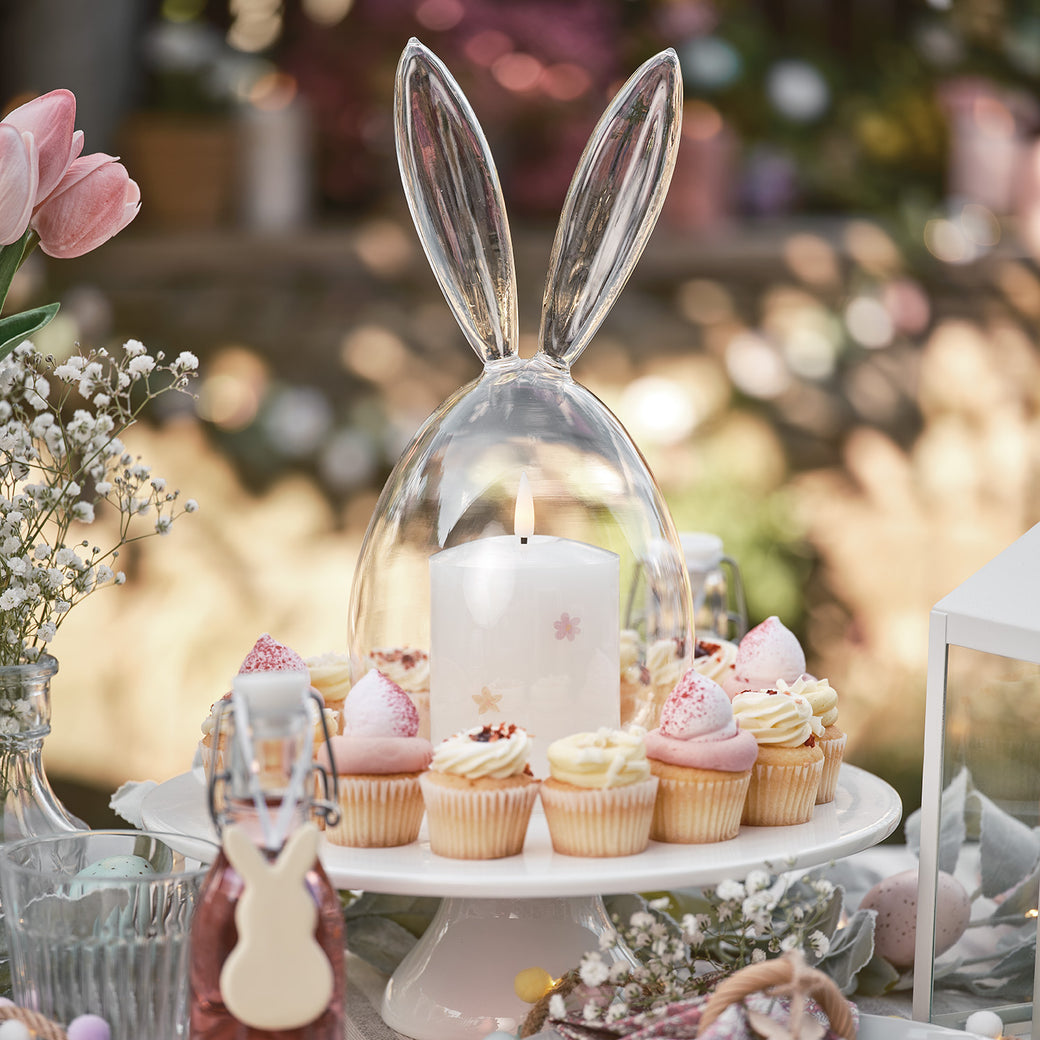 A cake stand with cupcakes and a LED candle under a glass bunny dome
