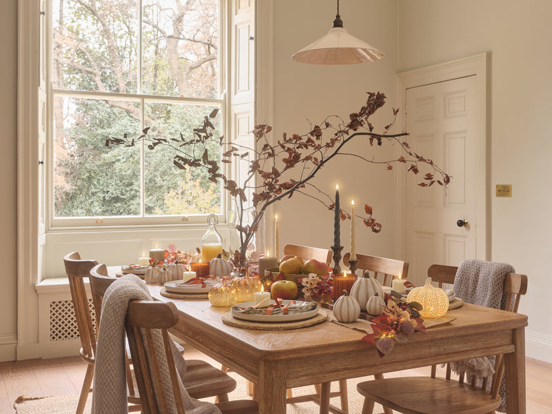 Dining table set with LED candles, porcelain and glass pumpkins, and autumnal foliage