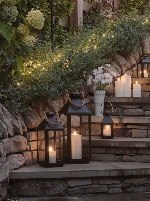 A garden at night with glowing lanterns and LED candles on steps underneath fairy lights