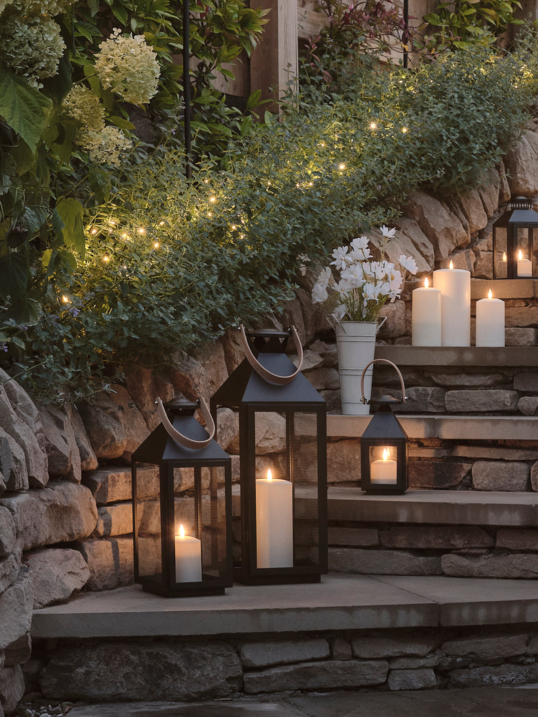 A garden at night with glowing lanterns and LED candles on steps underneath fairy lights