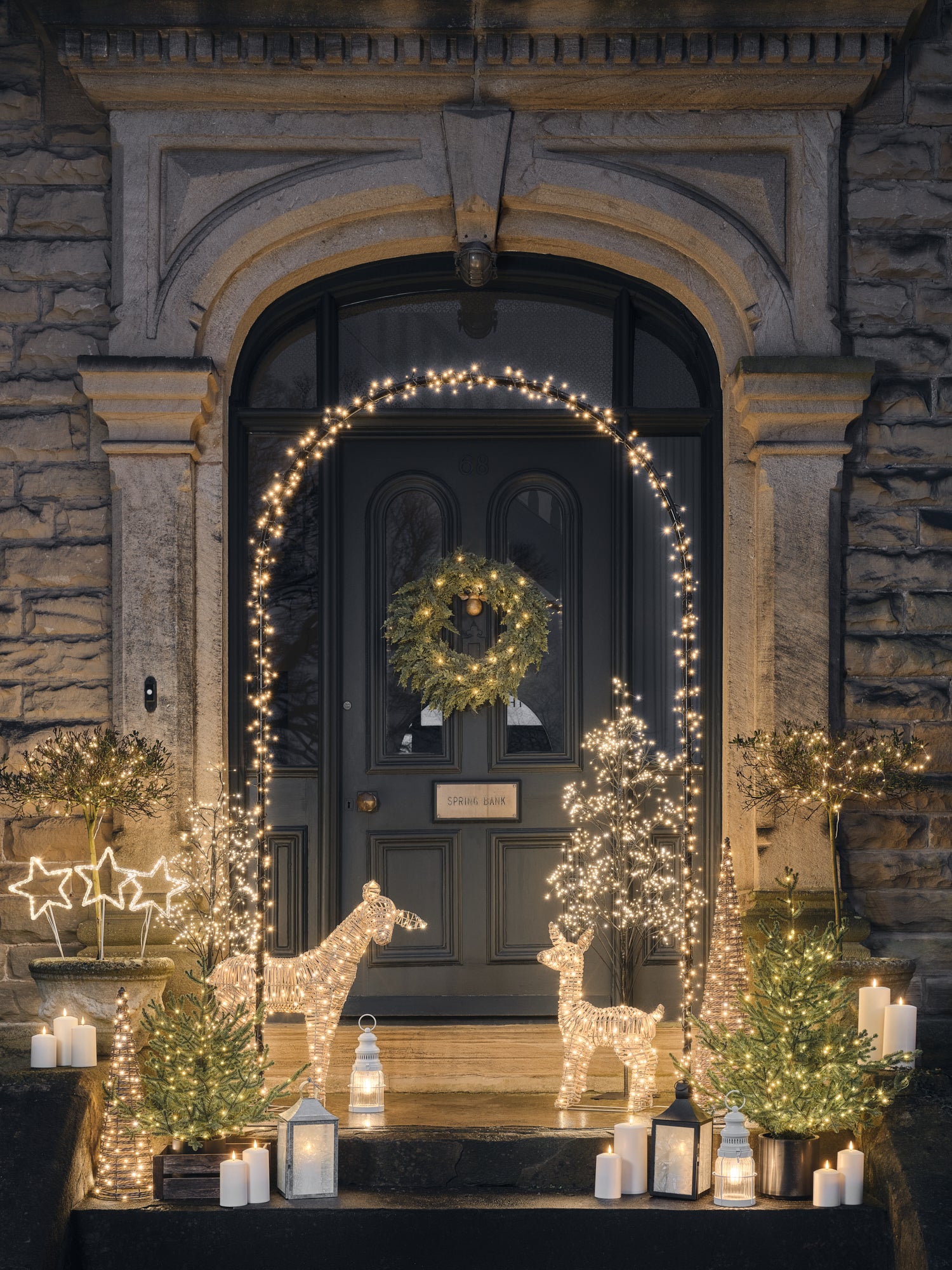 Front door decorated with LED candles, lanterns, reindeer, and foliage