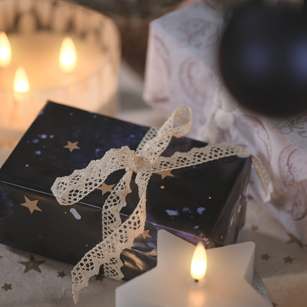 A Christmas present wrapped in dark blue starry paper with a white lace bow
