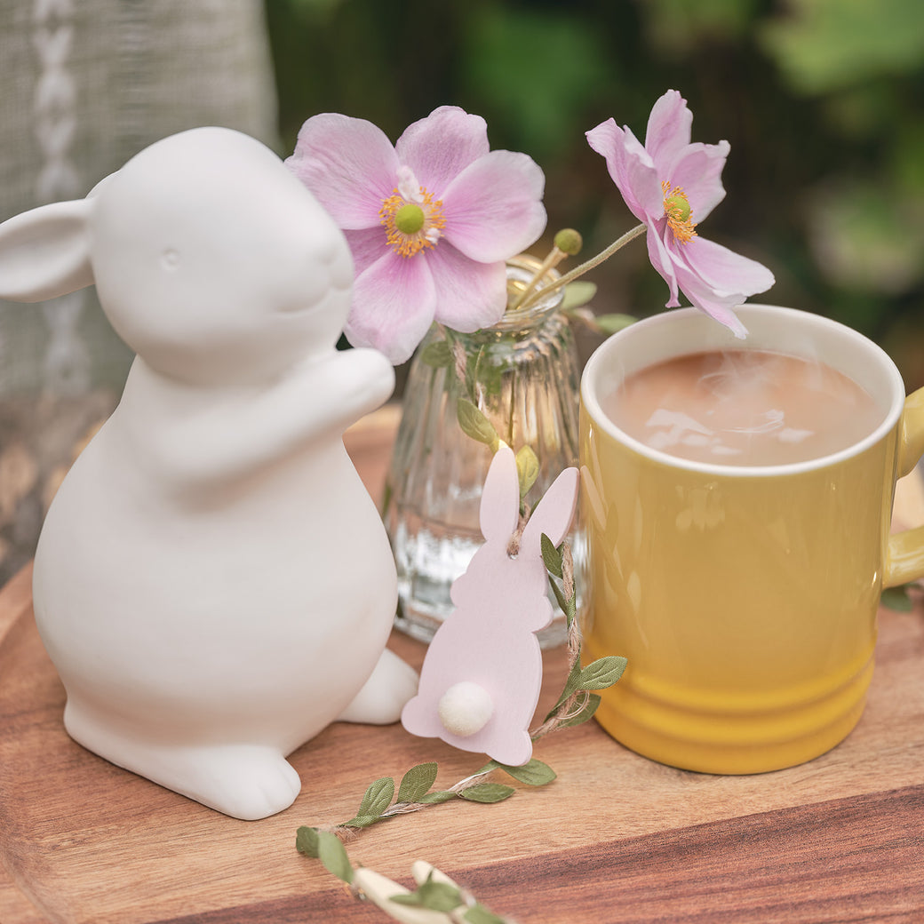 Porcelain bunny on a table with a wooden bunny garland, vase of flowers, and cup of tea 