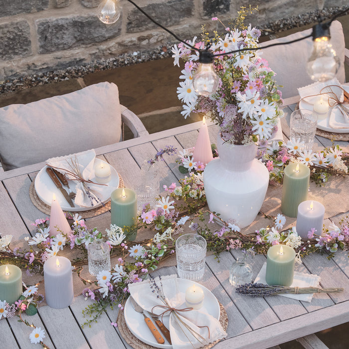 Festoon lights hanging above a set outdoor dining table with a bouquet of pink and white flower in a vase