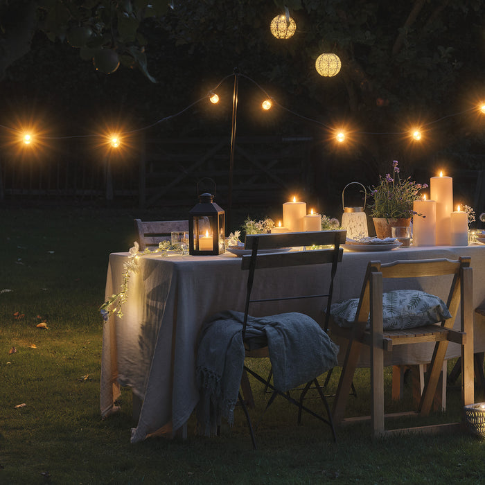Warm festoon lights hang above an outdoor dining table at night