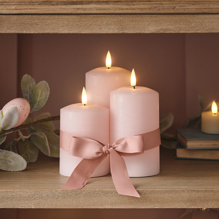 Pink LED candle trio of different sizes with a ribbon wrapped around them in a bow