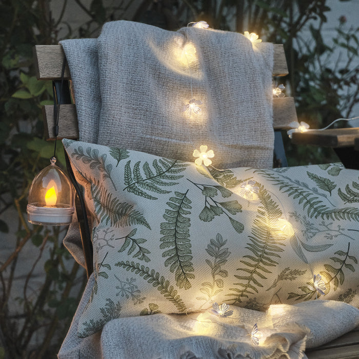 Blue and yellow flower shaped fairy lights draped over a wooden chair with a cushion and blanket