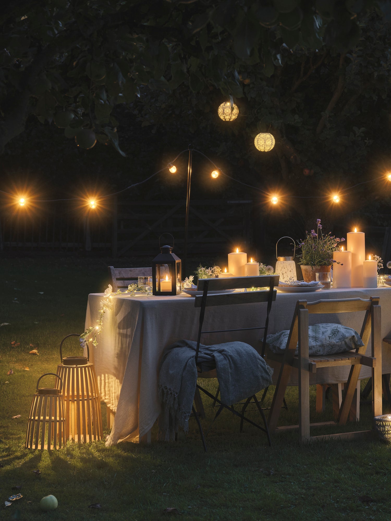 Festoon lights hanging above an outdoor table set with lanterns and candles