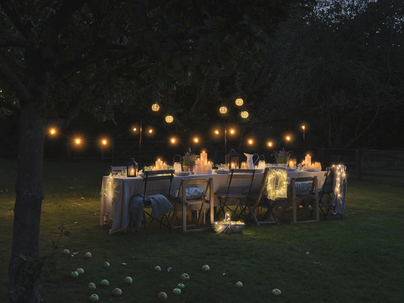 Outdoor dining table set with LED candles and lanterns underneath festoon lights