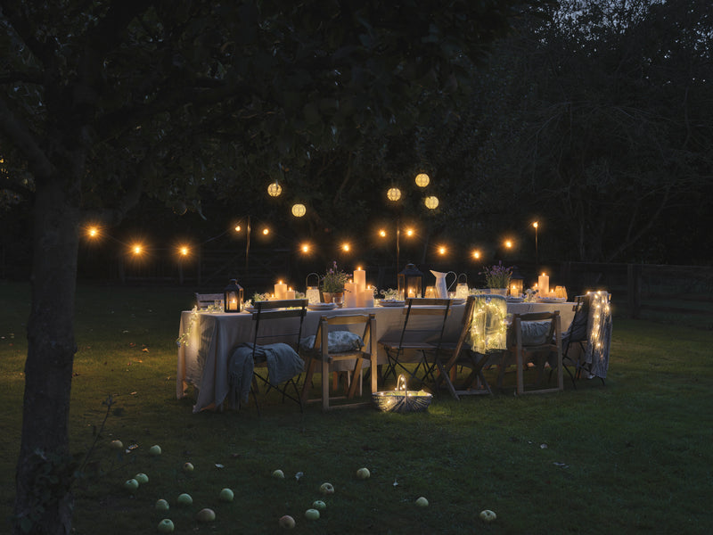 Outdoor dining table set with LED candles and lanterns underneath festoon lights