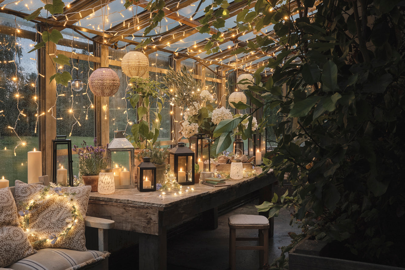 A greenhouse decorated with lanterns, fairy lights, and floral wreaths and garlands