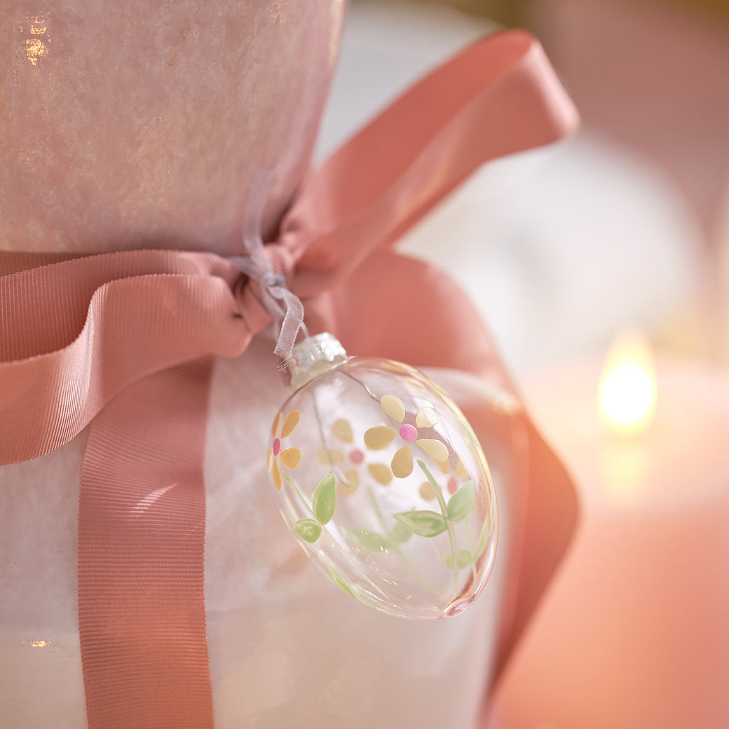 Glass easter egg decoration hanging from a bow wrapped around a vase