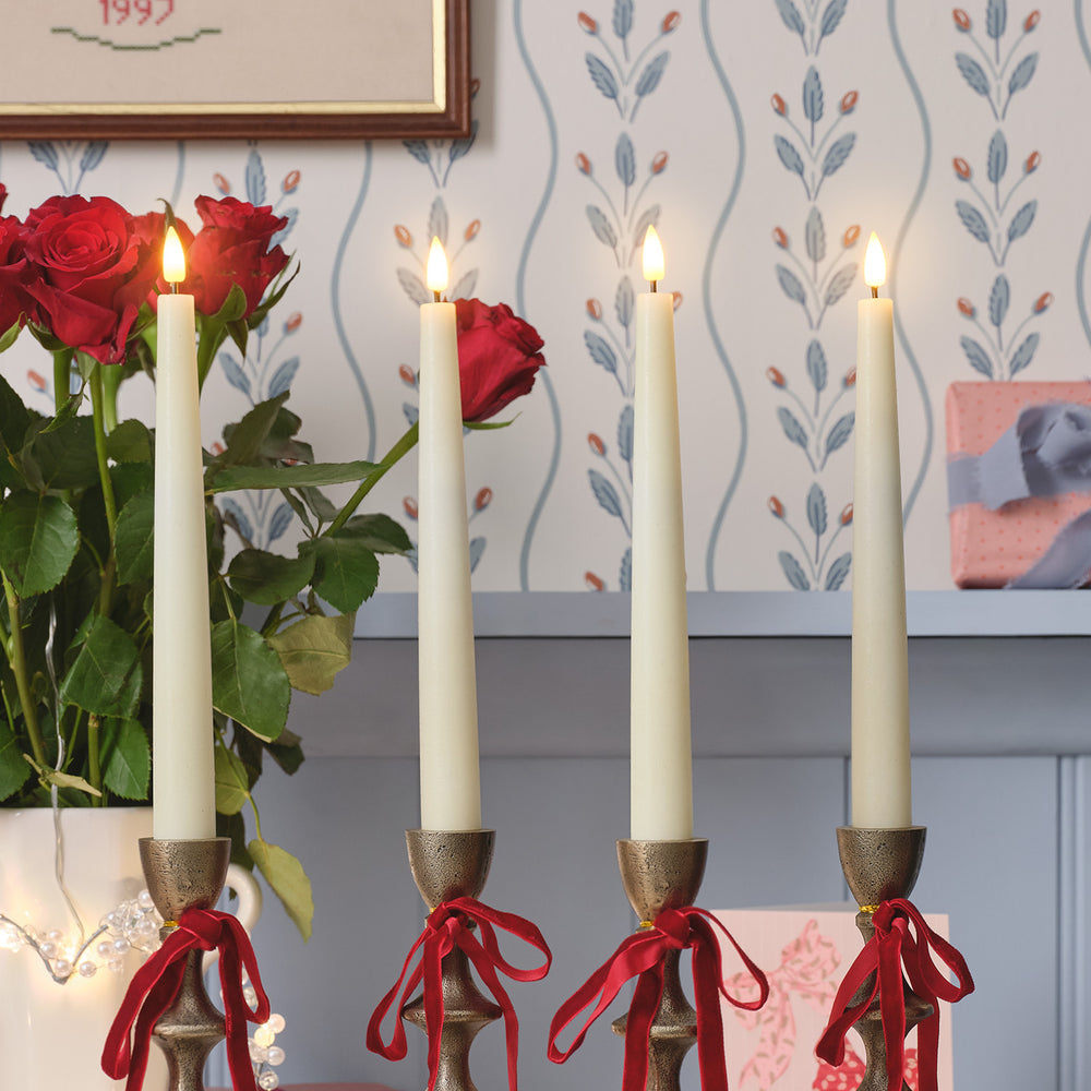 4 ivory taper candles in candle holders with ribbons wrapped in bows around them