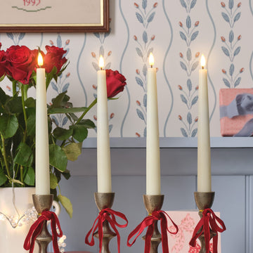 4 ivory taper candles in candle holders with ribbons wrapped in bows around them