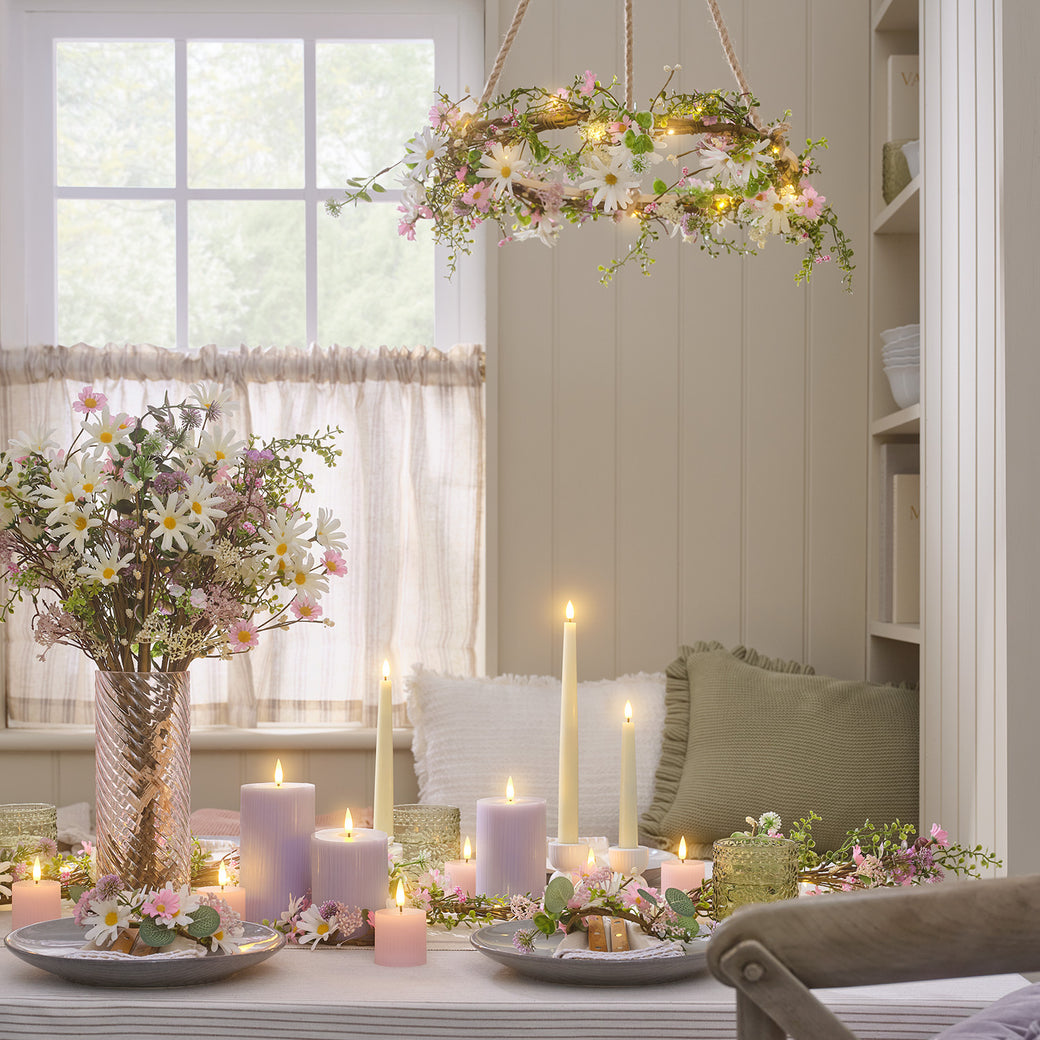 A dining table with a daisy bouquet and wreaths, and LED candles