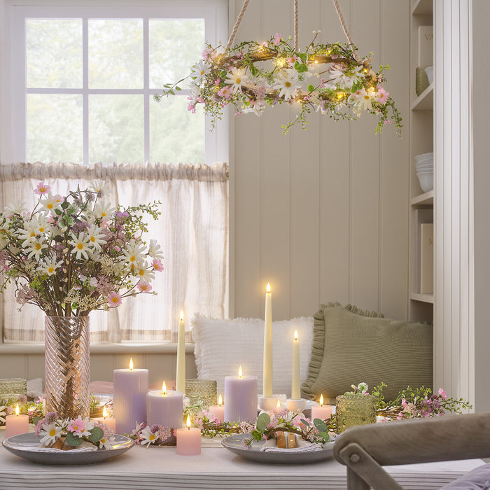 A dining table with a daisy bouquet and wreaths, and LED candles