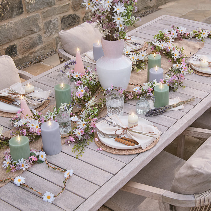 Outdoor dining table with place settings, LED candles, floral garlands, and a vase of flowers