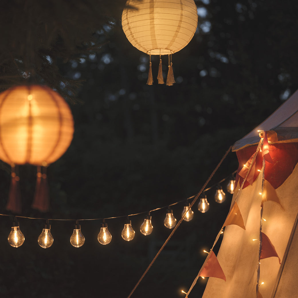 Lanterns hanging from tree branches above festoon lights