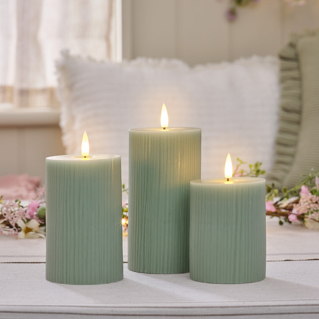 Three pastel sage green LED candles on a dining table