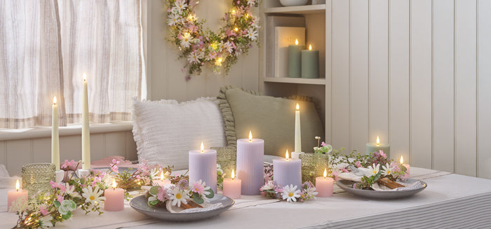 A dining table set with floral garlands, place sets, and pastel pink and lilac LED candles
